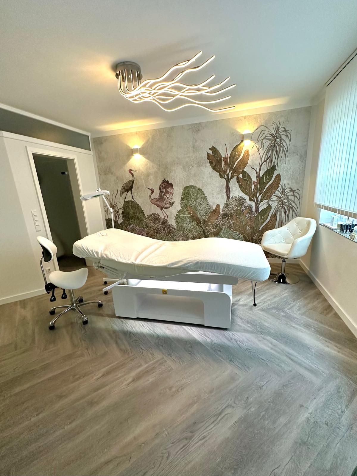Der Behandlungsraum im Kosmetikstudio Art of Style in Burbach: weiße Behandlungsliege vor einer Wand mit Reihern und Pflanzen